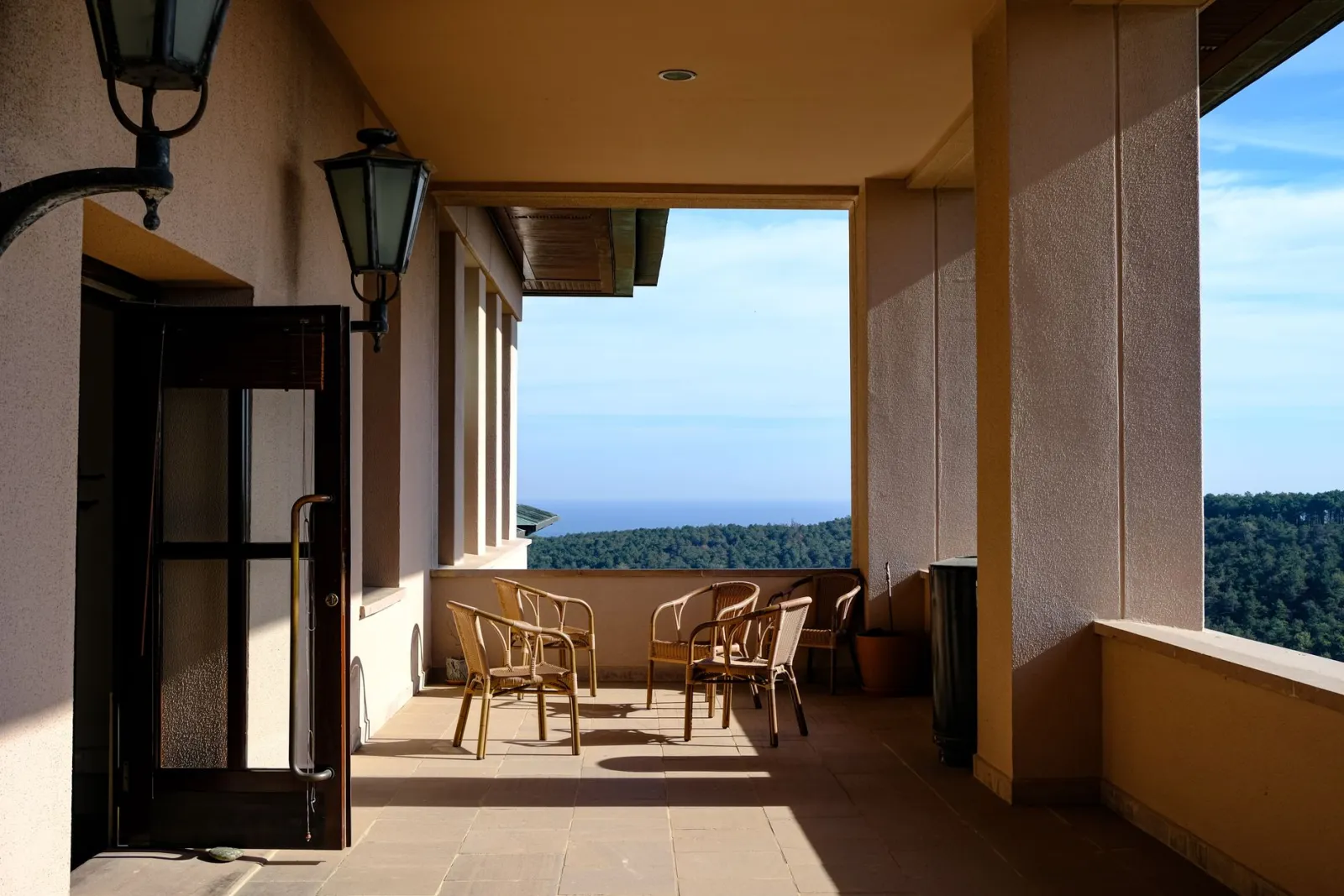 Peaceful terrace with chairs and shadows overlooking a scenic landscape.